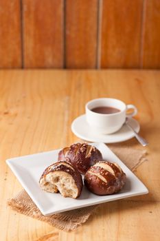 Freshly baked soft pretzel with generous sprinkling of coarse salt on white dish and a cup of hot chocolate in background