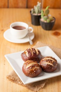 Freshly baked soft pretzel with generous sprinkling of coarse salt on white dish and a cup of hot chocolate in background