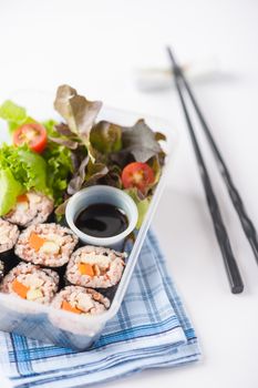Japanese style brown rice maki with grilled chicken, grilled pork, and grilled tofu cooked by clean food concept in lunch box on white table