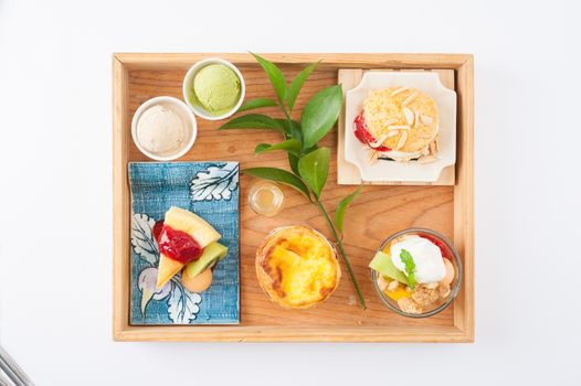 Dessert set for tea time with cake, ice cream, egg tart, and scone in wood tray on white table