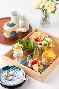 Dessert set for tea time with cake, ice cream, egg tart, and scone in wood tray on white table with tea set and diashes