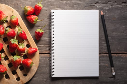 Strawberries and notebook on wood background in vintage style with low key scene.