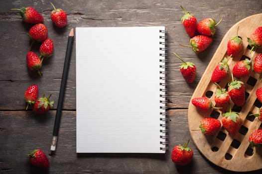Strawberries and notebook on wood background in vintage style with low key scene.