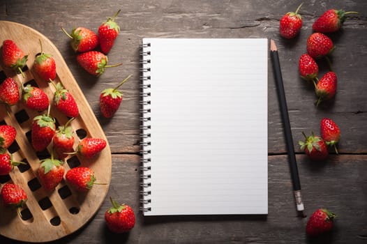 Strawberries and notebook on wood background in vintage style with low key scene.