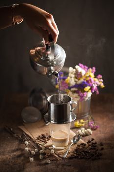 Vietnamese style drip coffee, Woman hand pouring hot water into metal coffee filter with low key scene