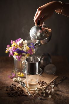 Vietnamese style drip coffee, Woman hand pouring hot water into metal coffee filter with low key scene