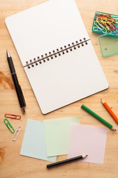 Notebook and sticky paper, paper clip, color pencil, and pen on wood table