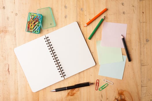 Notebook and sticky paper, paper clip, color pencil, and pen on wood table