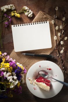 Small notepad with pen, pencil and bits of red velvet cake on rustic wood background with low key scene.