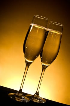 two champagne glasses with bubbles on golden background