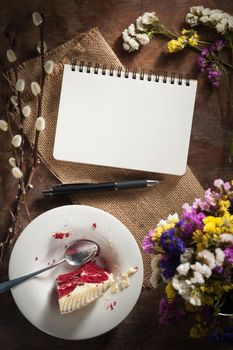 Small notepad with pen, pencil and bits of red velvet cake on rustic wood background with low key scene.