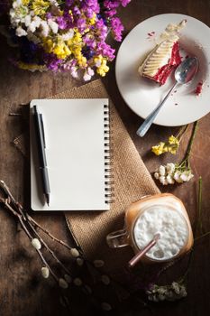 Notepad with pen, a glass of Thai tea and bits of red velvet cake on rustic wood background with low key scene