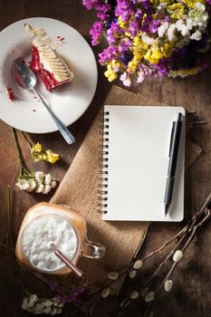 Notepad with pen, a glass of Thai tea and bits of red velvet cake on rustic wood background with low key scene