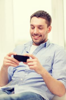 home, technology and internet concept - smiling man with smartphone sitting on couch at home