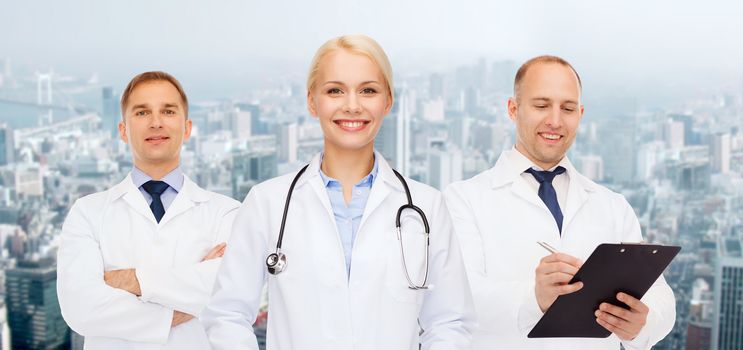 healthcare, people and medicine concept - group of doctors with stethoscopes and clipboard over city background