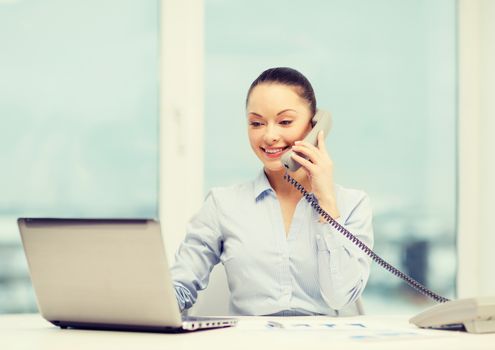 business, technology and communication concept - smiling businesswoman with phone, laptop and files in office