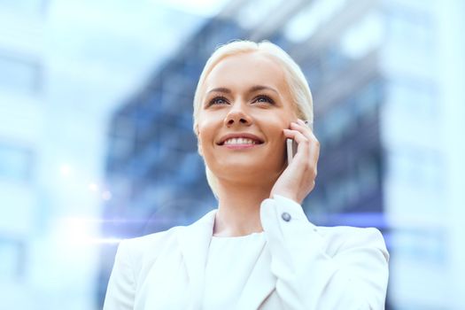 business, technology and people concept - smiling businesswoman with smartphone talking over office building