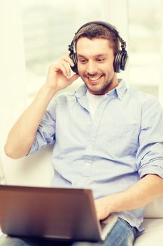 technology, home, music and lifestyle concept - smiling man with laptop and headphones at home