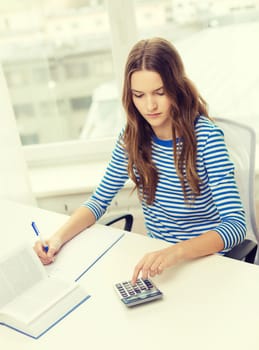 education and home concept - concentrated student girl with notebook, calculator and book