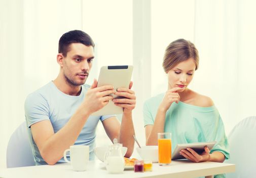 food, home, couple and technology concept - concentrated couple with tablet pc reading news and having breakfast at home