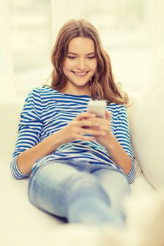 home, technology and internet concept - smiling teenage girl with smartphone lying on couch at home