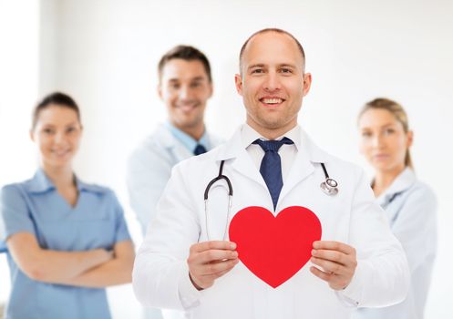 medicine, profession, charity and healthcare concept - smiling male doctor with red heart and stethoscope over group of medics