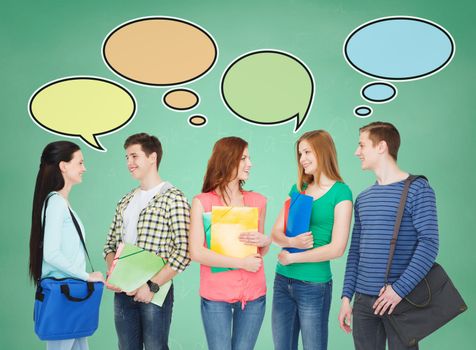 school, education, communication and people concept - group of smiling teenagers with folders and school bags talking over green board background with text bubbles