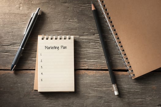 Small notepad with pen and pencil on rustic wood background with low key scene.
