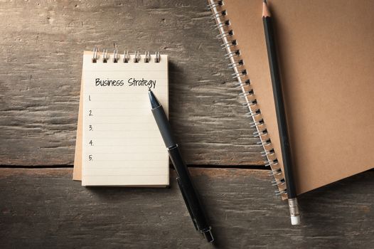 Small notepad with pen and pencil on rustic wood background with low key scene.