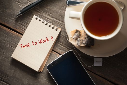 Small notepad with written messeage,  a cup of tea, pen, pencil and cellphne on rustic wood background with low key scene