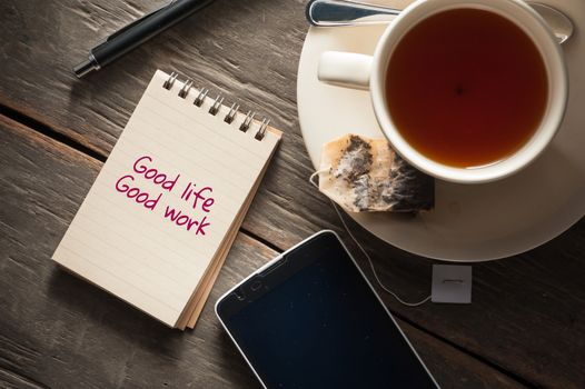 Small notepad with written messeage,  a cup of tea, pen, pencil and cellphne on rustic wood background with low key scene