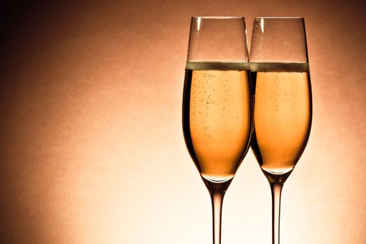 two glasses of champagne with golden bubbles and space for text against brown background