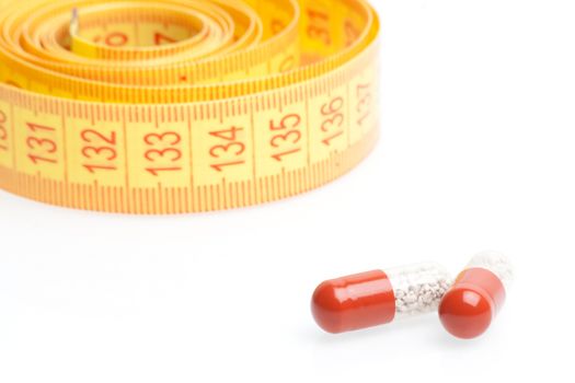 medical pills for dieting in front of measuring tape on a white background