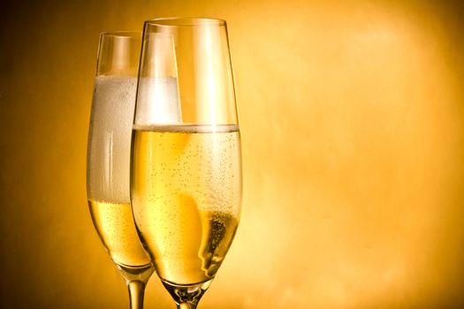 two flutes of champagne with golden bubbles and white foam against golden background
