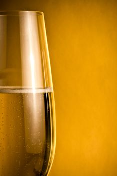 half glass of champagne with golden bubbles against golden background