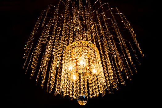 a crystal chandelier glows with golden light on dark background