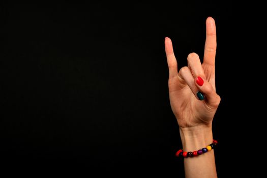 Female hand with devil horns rock metal sign symbol gesture and colorful wooden beads isolated on black background