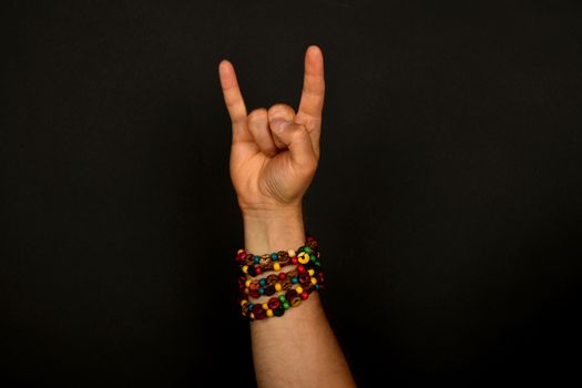 Male hand with devil horns rock metal sign symbol gesture and colorful wooden beads isolated on black background