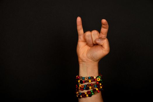 Male hand with devil horns rock metal sign symbol gesture and colorful wooden beads isolated on black background