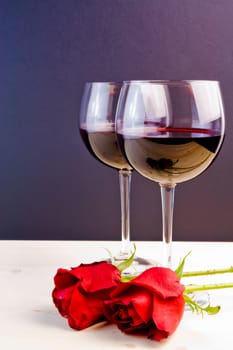 glasses of wine near red roses on old wood