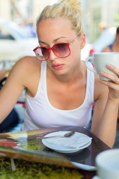 Calm casual blond lady enjoying cup of coffee outdoor in typical italian  street coffee house on warm summer day.