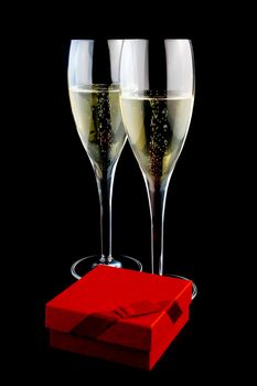 two glass with champagne near a gift on a black background