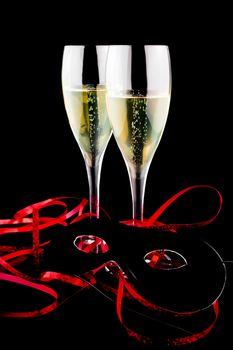 two flutes with champagne near a carnival mask on black background