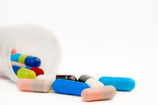 closeup of colored pills with unfocused bottle on white background