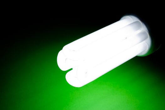 Close-up of glowing energy-saving light bulb on green background