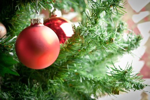 red christmas ornament hanging with unfocused ball and tree in background