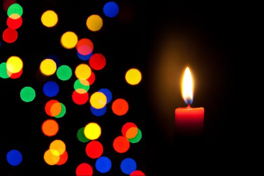 detail of red candle with defocused colorful lights on black background