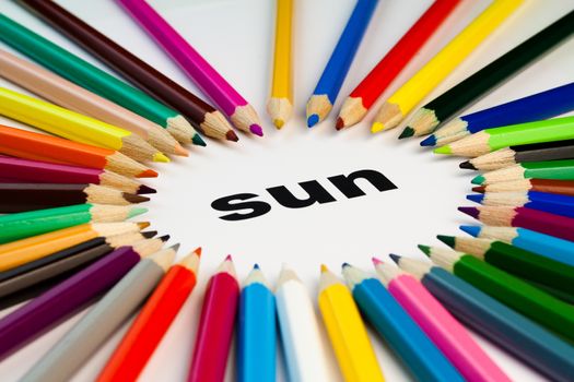 Detail view of many colored pencils arranged in circle on the word sun