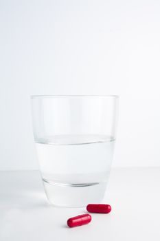 detail of red pills next to a water glass isolated on white background