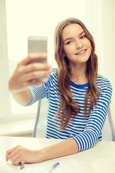 education, technology and home concept - happy smiling student girl with smartphone and textbook at home